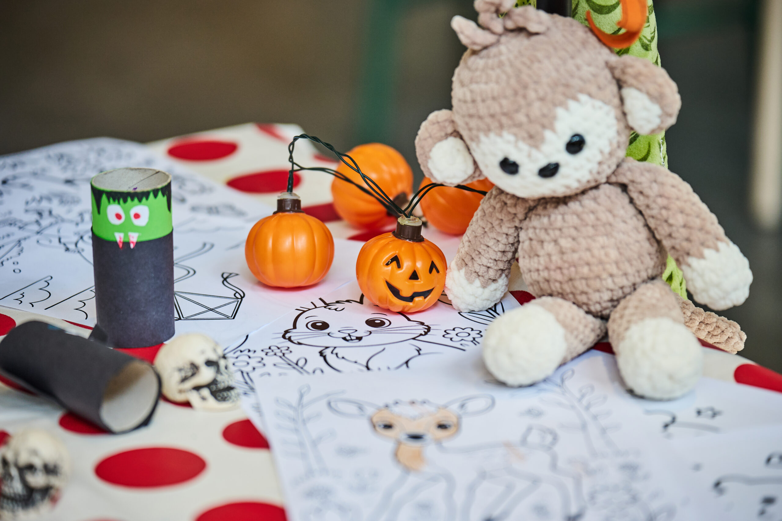 Halloween craft table with a crocheted monkey, pumpkin lights, and coloring sheets.